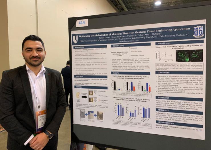 Saman Firoozi stands next to his poster