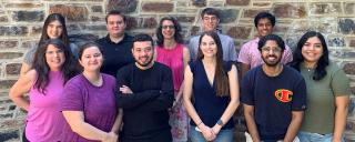 13 members of the lab team posing in front of a duke brick wall